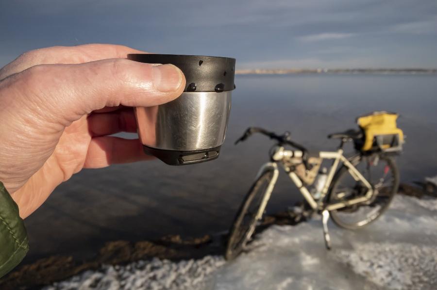 Radfahrer trinkt aus Thermoskanne - Fahrrad steht im Schnee an einem See - Radtour im Winter
