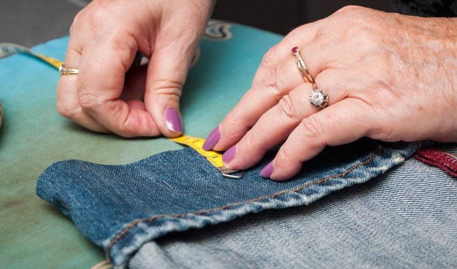 Eine Frau näht eine Jeans um - Umrechnung von Normalgröße zu Kurzgröße
