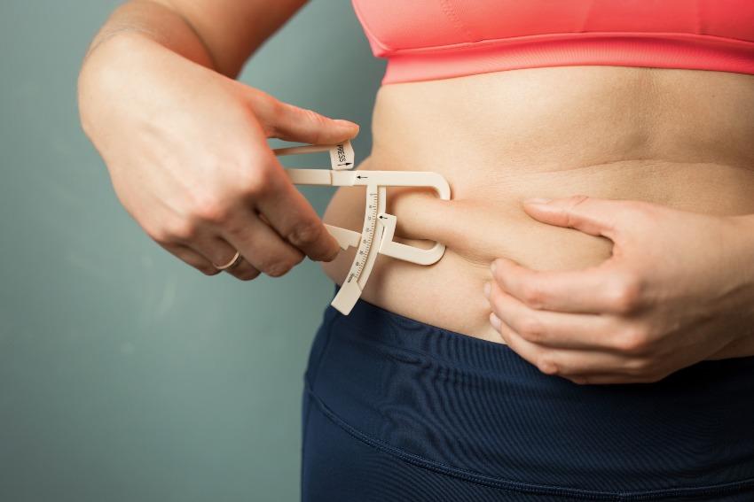 Frau misst mit Körperfettzange ihr Bauchfett - Sport für Übergewichtige
