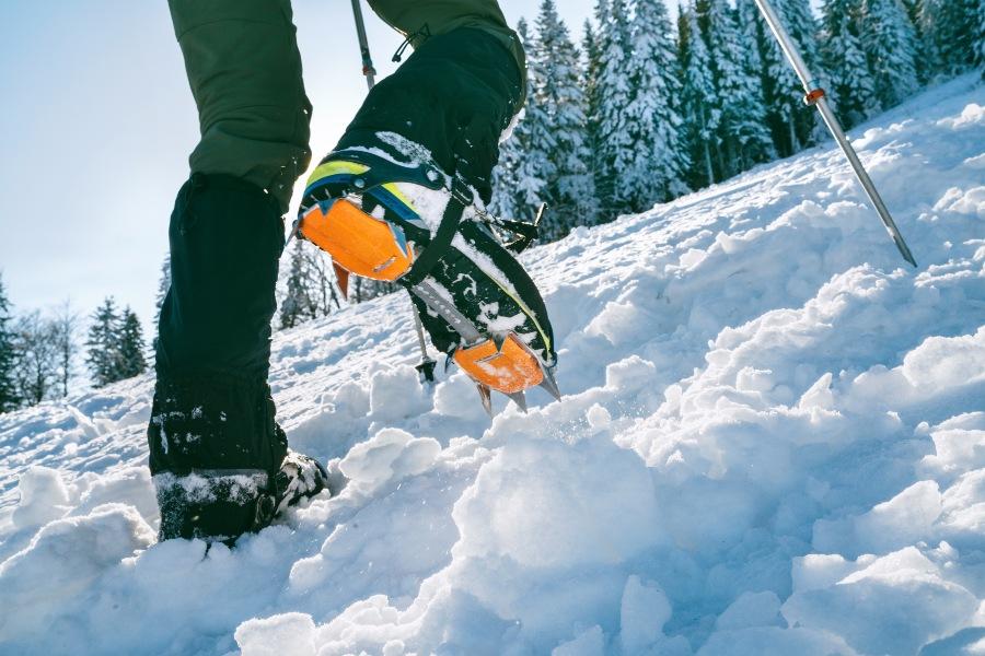 Mann stapft durch den Schnee mit Gamaschen und Spikes an den Schuhen