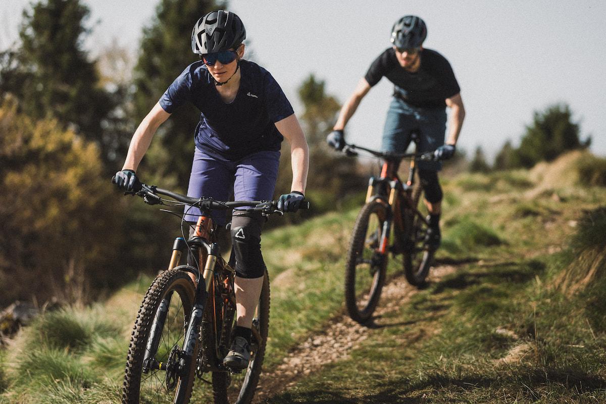 Zwei Gravelbiker fahren Hang hinunter. Beide stehen im Sattel und schauen konzentriert nach vorne.