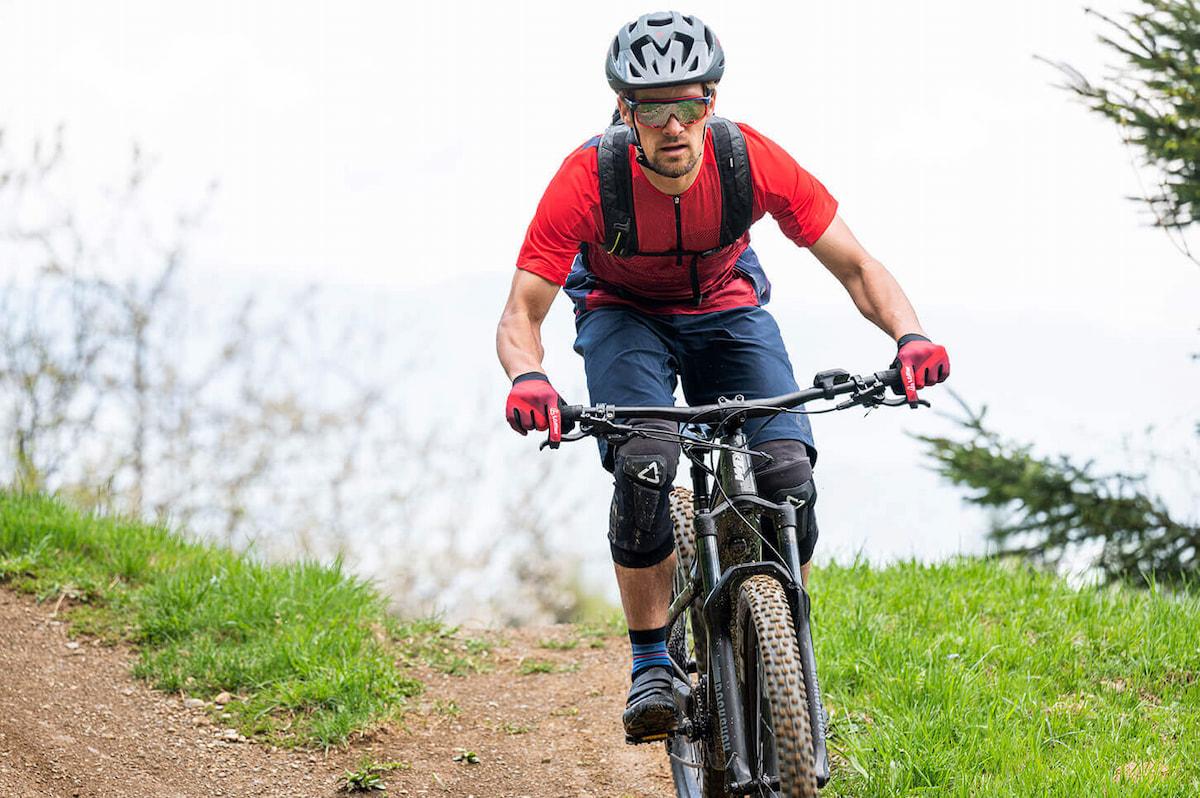 Durch enge Kanäle auf der Handinnenseite verlaufen zwei Nerven - werden diese durch Druck komprimiert, entstehen taube Hände. Mann mit roten Fahrradhandschuhen fährt Dirttrail runter
